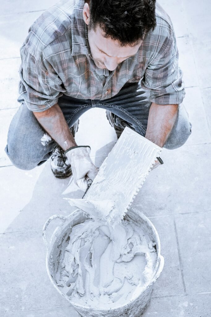 A mason prepares a bucket of cement with two spatulas to glue some tiles.